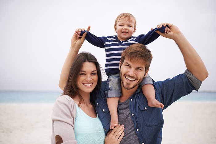 family of three smiling a beach